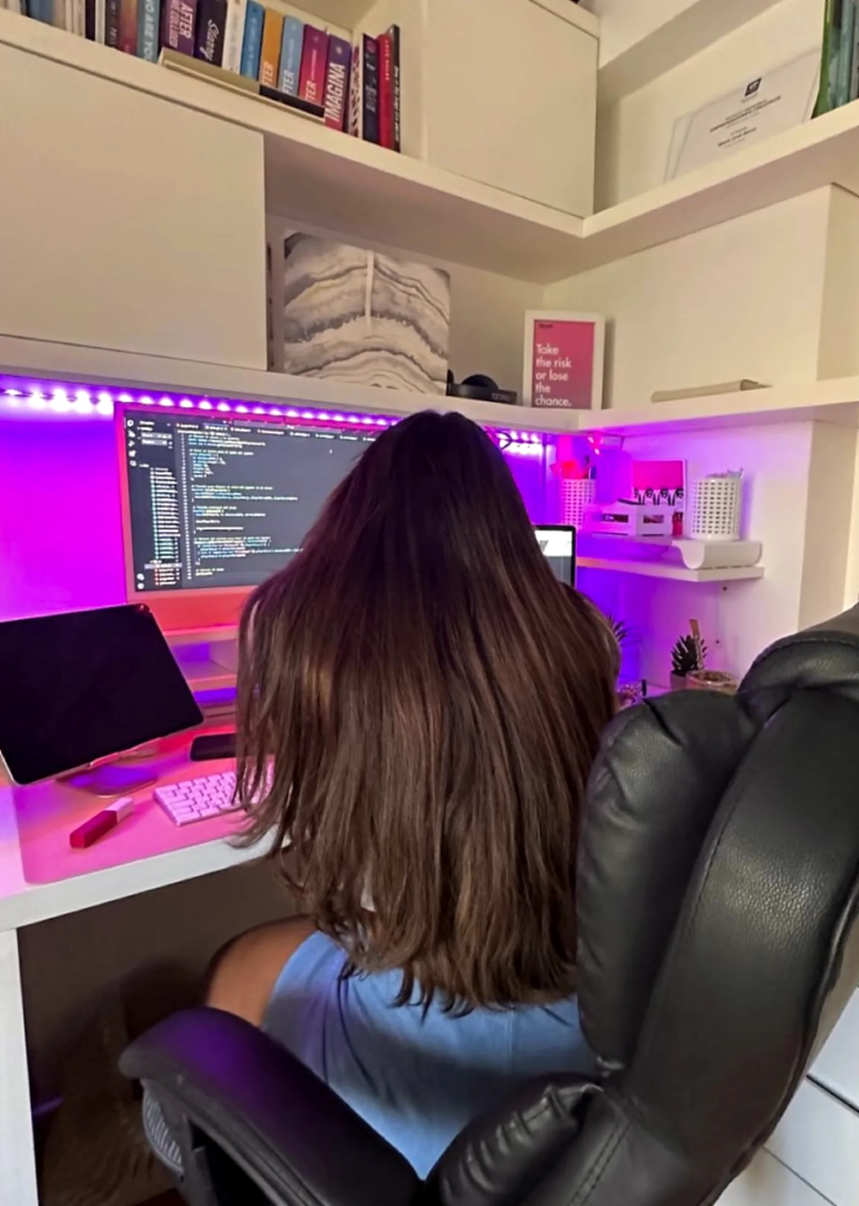 Majo de espaldas, programando en su escritorio con luz rosa y violeta