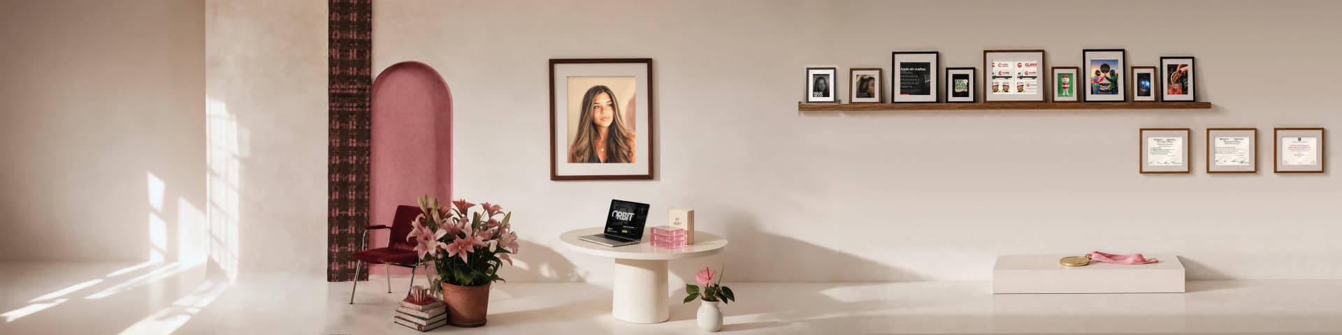 La sala del set de Majo: la ventana, la tela escocesa, el arco rosa con la silla bordó, las flores y sus apuntes, su retrato, la mesa con sus cuadernos y el libro By Majo, el estante con sus proyectos enmarcados, la medalla y sus diplomas.