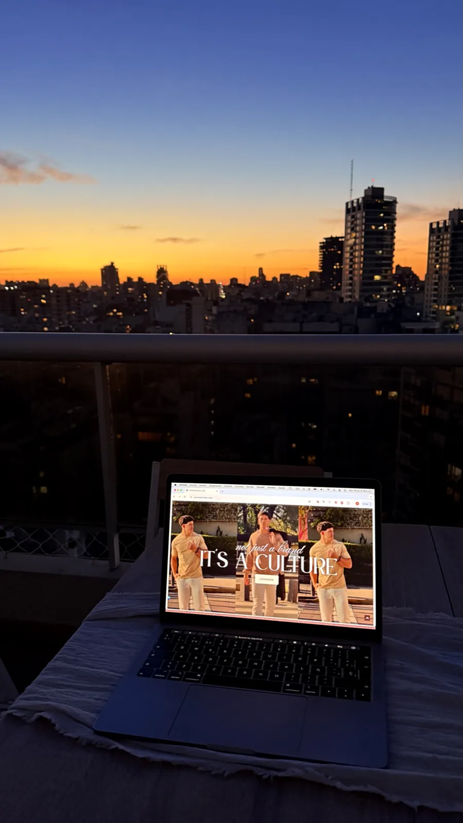 Su laptop en la terraza al atardecer, con la ciudad de fondo