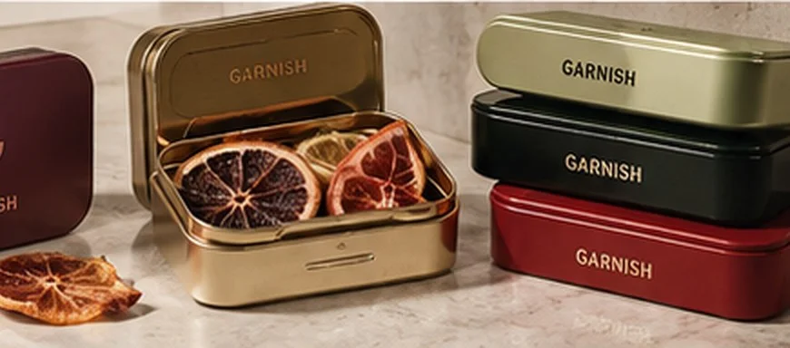 Mini latas Garnish en aubergine, dorado, oliva, negro y rojo, una abierta con rodajas de fruta